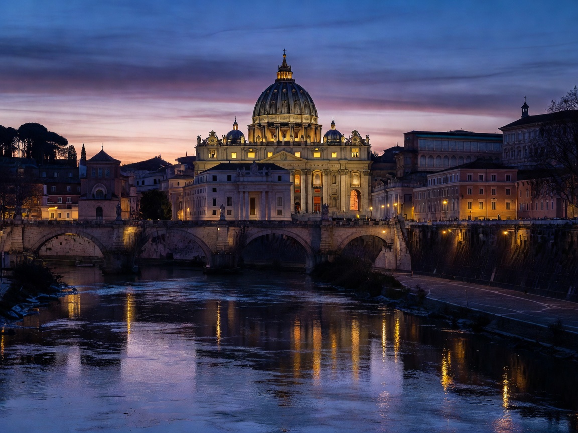 St Peters Basilica illuminated at twilight across the Tiber River in Rome